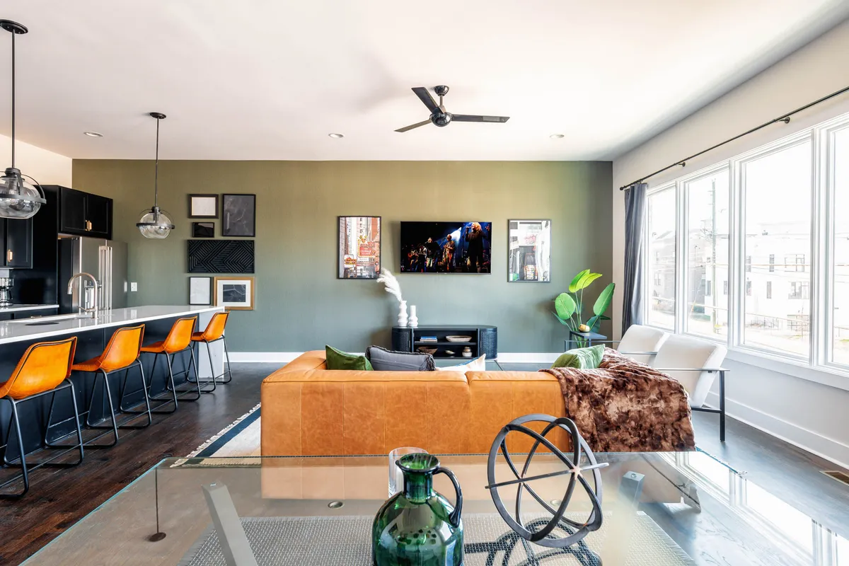 A harmonious open-concept space where the sofa, kitchen island, television, and large windows are all visible. Contemporary furnishings and decorative elements, such as plants, tie the living, dining, and kitchen areas together seamlessly.