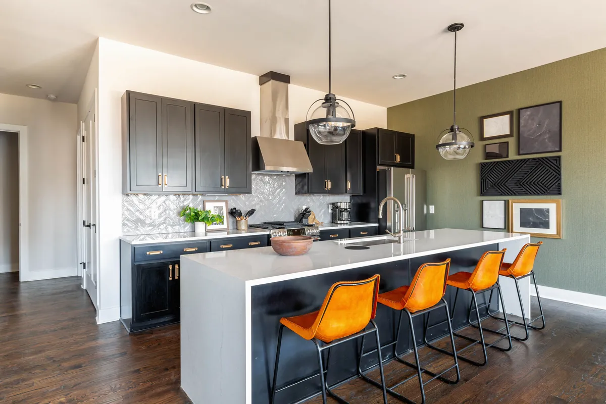 A modern kitchen anchored by a striking kitchen island with bar stools, decorative wall art, and contemporary finishes. The space is set up for both cooking and entertaining, with enough room for guests to gather around.