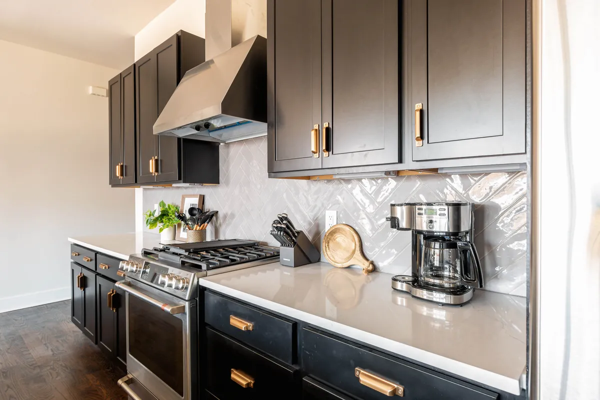 A modern kitchen space showcases stainless steel appliances, sleek black cabinetry, white countertops, and a decorative backsplash. The kitchen looks well-organized, inviting, and ready for family use or entertaining guests.