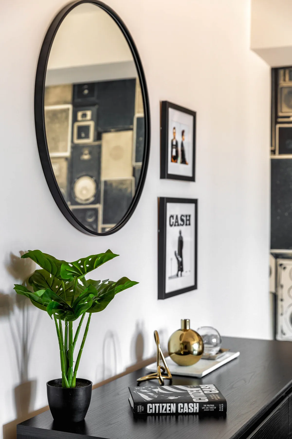 A stylish entryway features a round mirror, framed photos, decorative objects, books, and an inviting indoor plant. The space is neatly organized and welcoming, making it an ideal first impression area for guests.