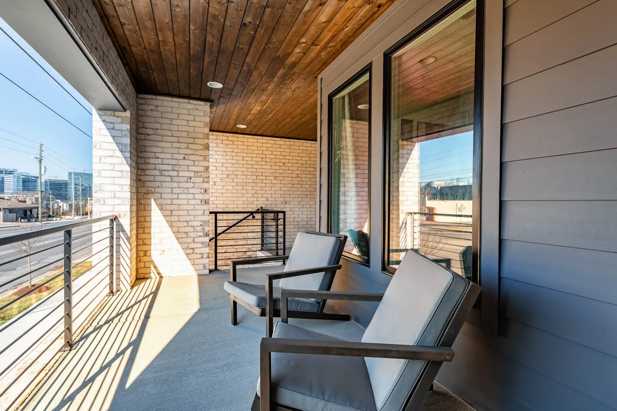This image features a cozy rooftop patio with two outdoor chairs, an exposed brick wall, wooden ceiling, and views overlooking the street. The ambient lighting and cityscape deliver a tranquil yet urban atmosphere, perfect for enjoying coffee or sunset cocktails.