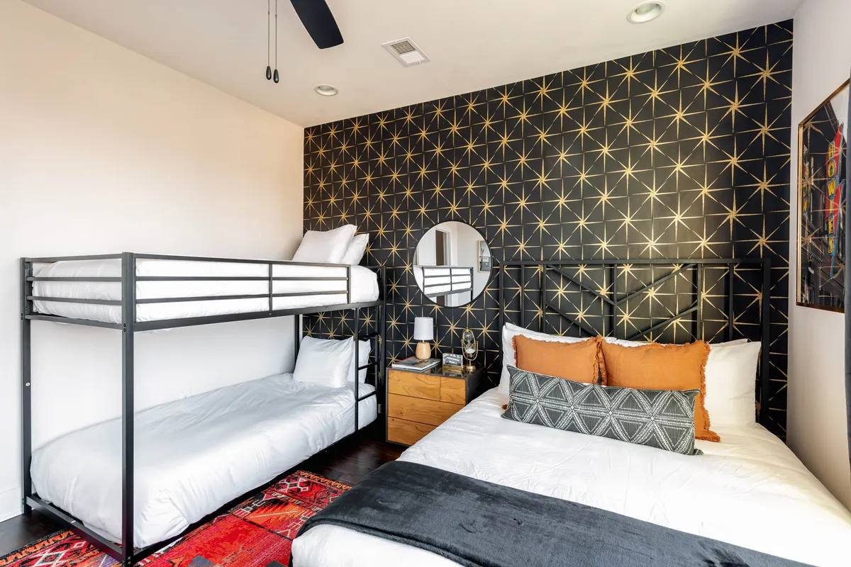 A playful kids’ bedroom features a bunk bed with decorative pillows, a round mirror, and lively geometric wallpaper. The atmosphere is welcoming and fun, perfect for children or family travelers.