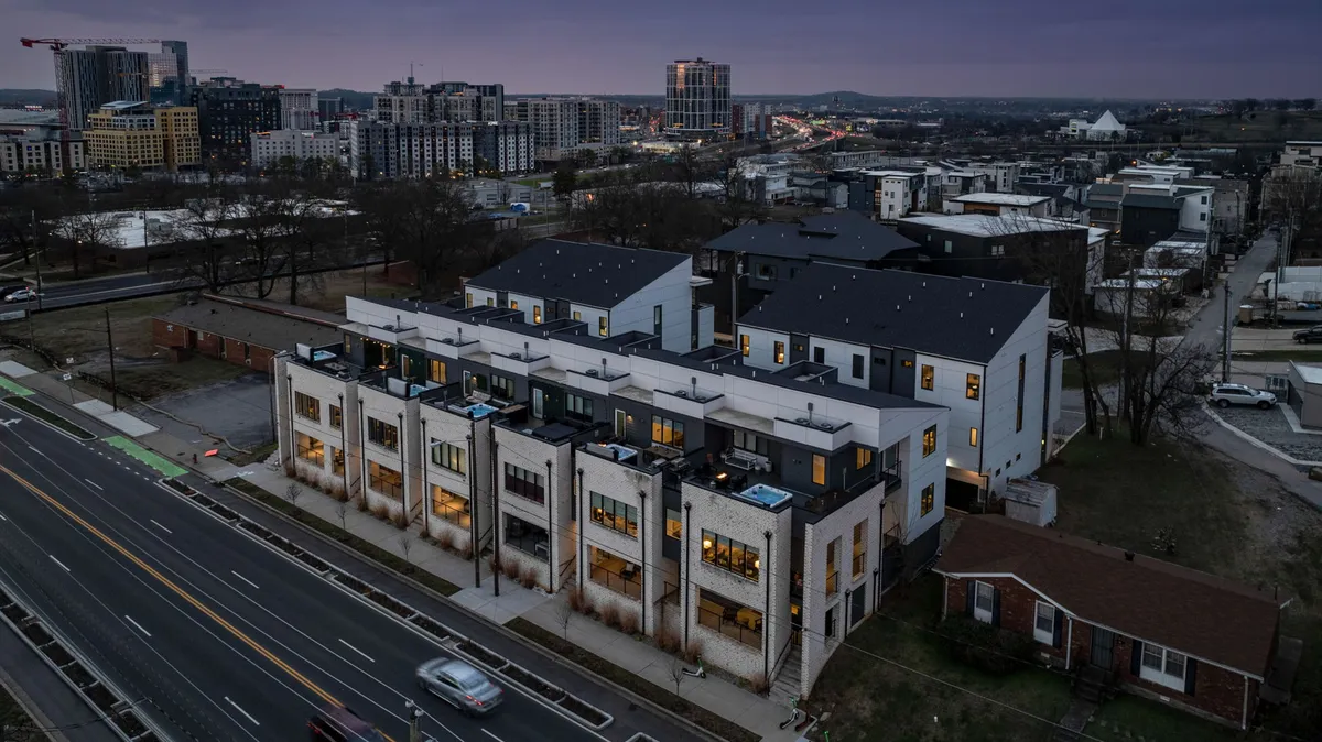 A set of contemporary townhomes with rooftop patios, the city skyline in the distance, and vehicles along the lit street. The scene captures the lively urban environment and the unique rooftop perspective available in The Gulch.