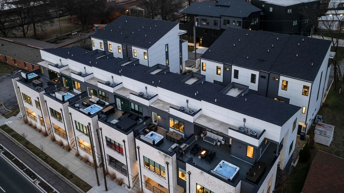 A contemporary rooftop terrace featuring outdoor seating arrangements and scenic city views. The space includes hot tubs and modern architectural elements, framed by the urban skyline in the background. Groups can be seen gathering and relaxing on the terrace, highlighting the social and luxurious atmosphere.
